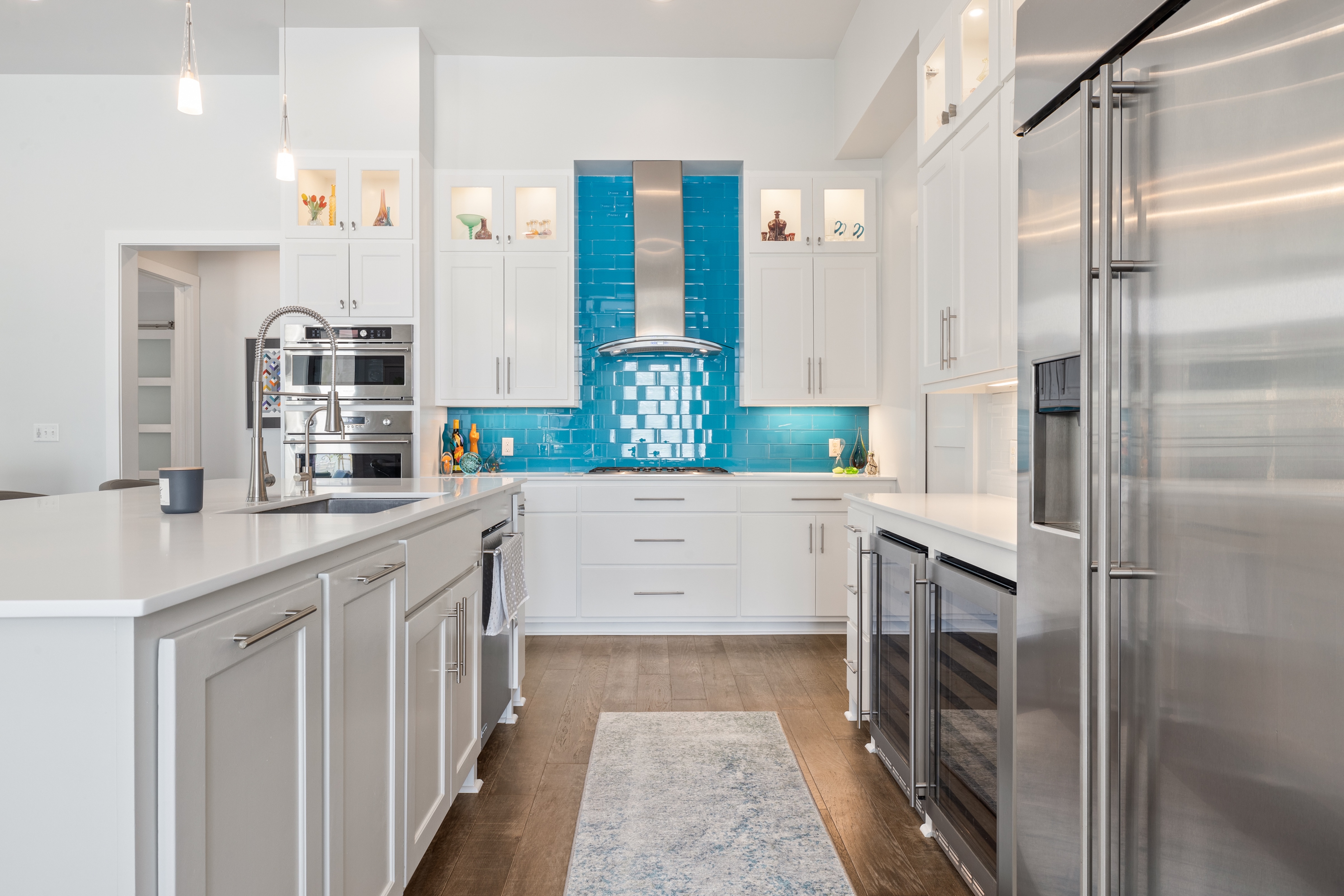 The open-concept kitchen features streamlined cabinetry, stainless appliances, and a striking turquoise tile backsplash that serves as a playful focal point.