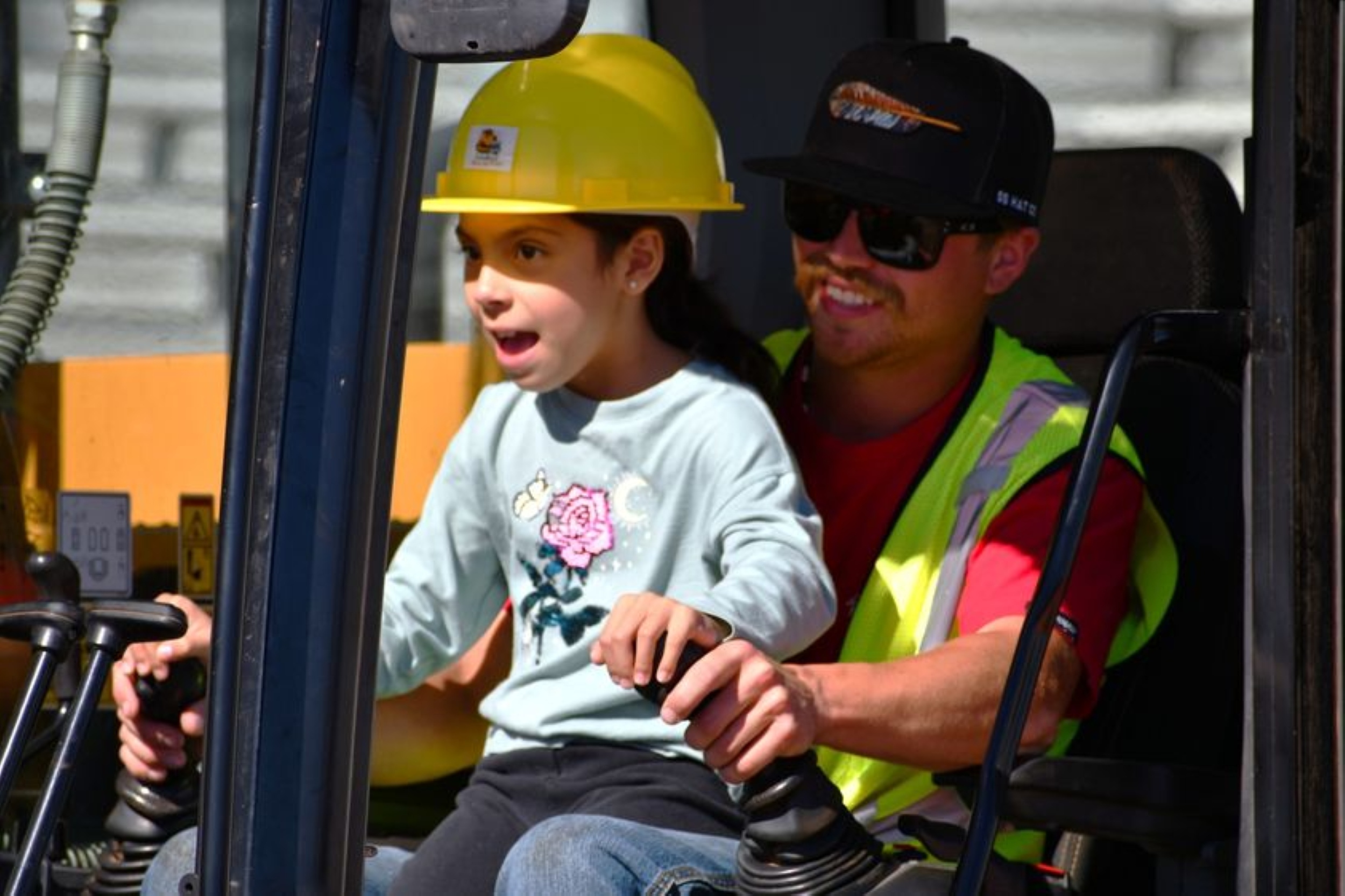 A young operator takes the controls of a real excavator with guidance from a trained construction professional during Dozer Day®, one of the Pacific Northwest's premier family events focused on education, exploration, and workforce development.